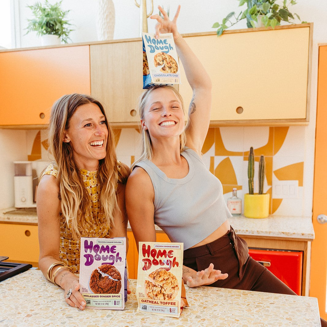 2 Women laughing and smiling while holding Home Dough bags